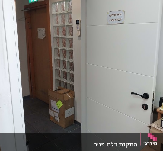 דלת לבנה פתוחה עם ידית שחורה ושלט אזהרה
